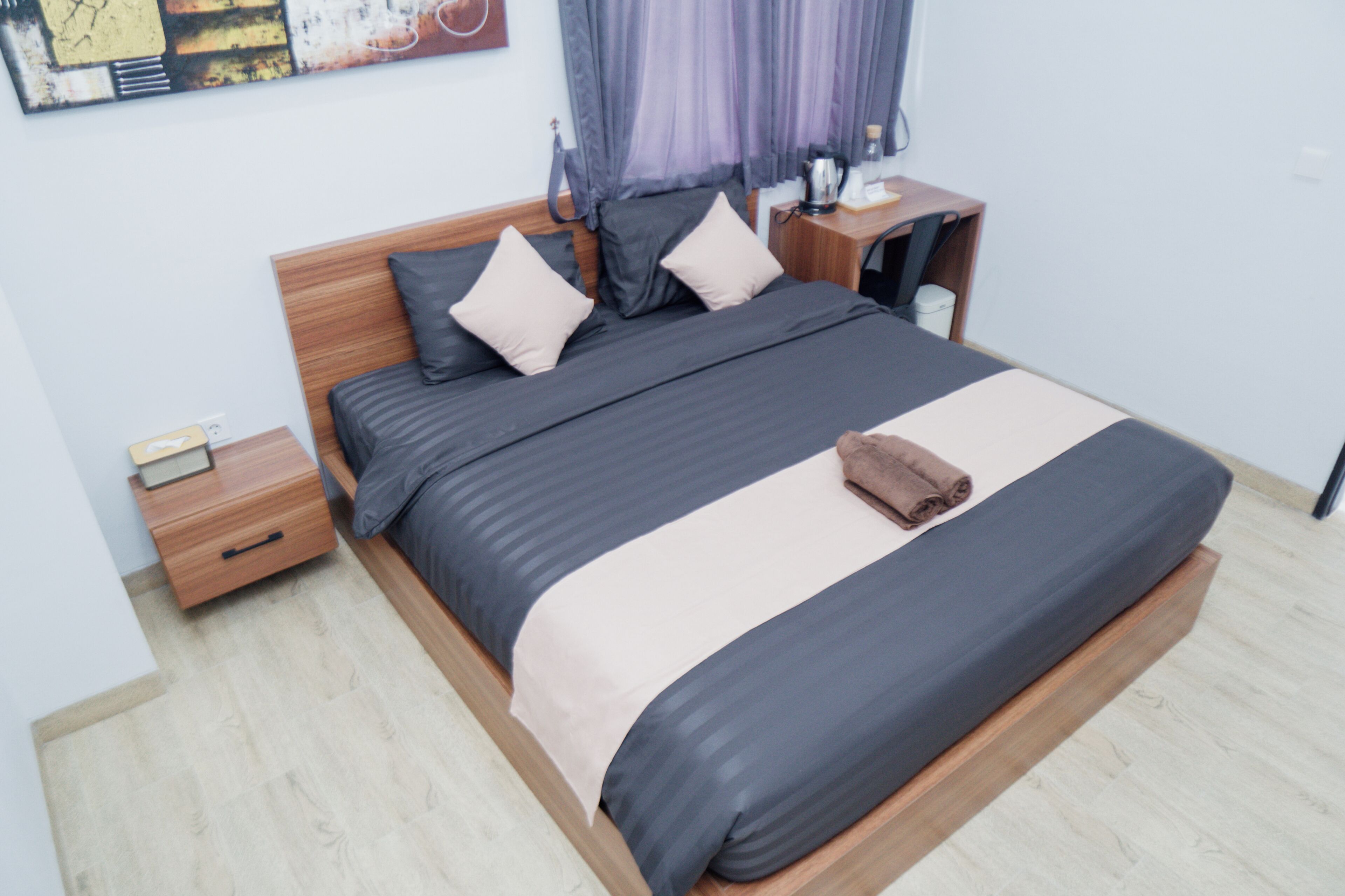 Una cama bien hecha con cabecera de madera, una mesita de noche con lámpara y una obra de arte colgada en la pared.