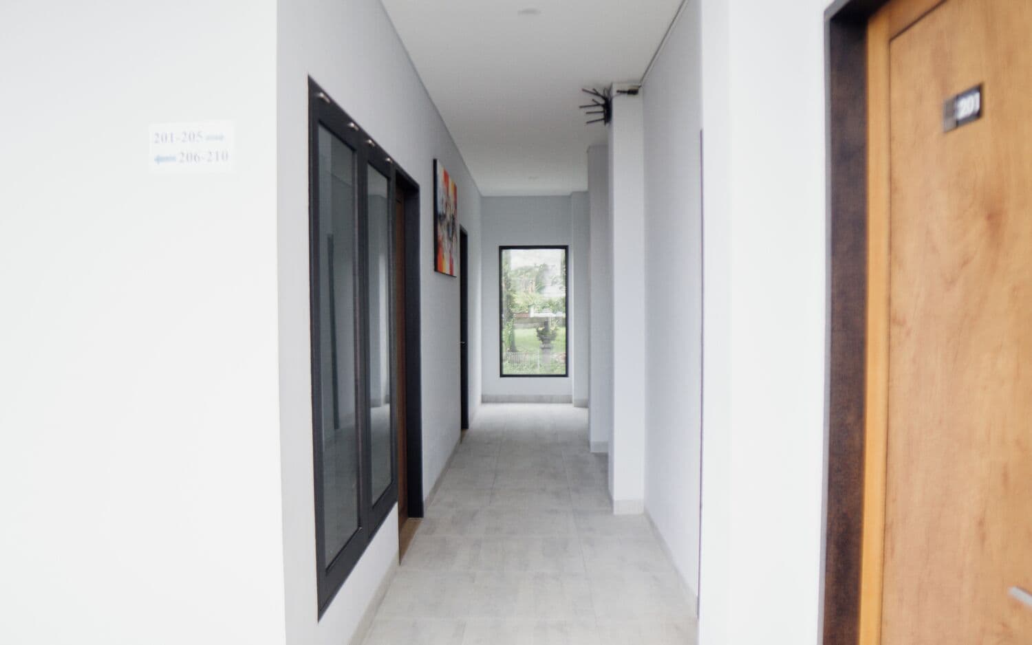 Un pasillo con una puerta de madera, una puerta de cristal y vistas de un jardín a través de un ventanal grande.