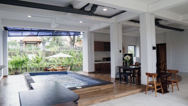 A spacious indoor area with a hot tub, dining table, and chairs, and a view of a garden through large windows.