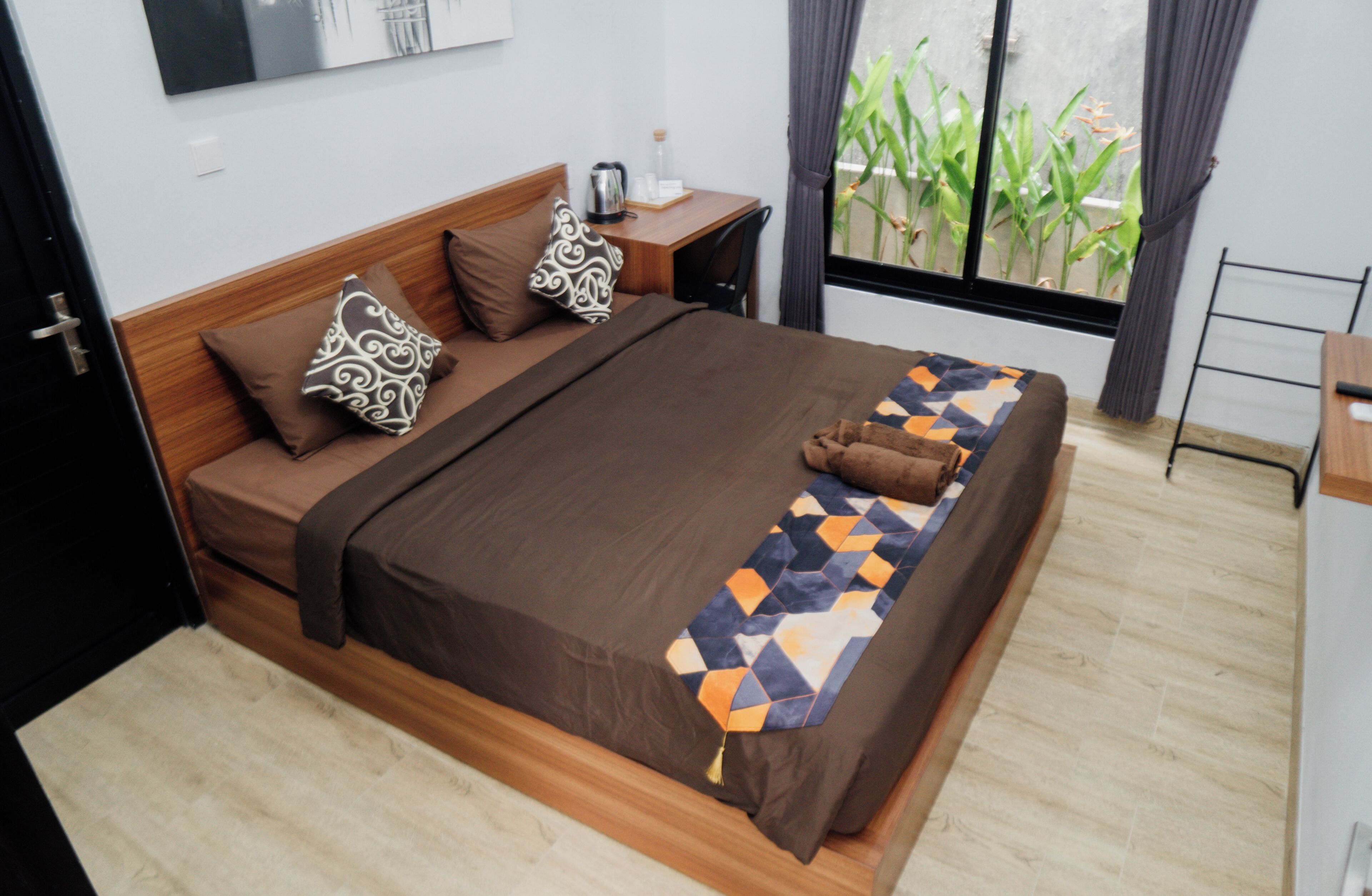 A neatly made bed with a patterned blanket, a wooden headboard, and a small bedside table with a lamp and a bottle.