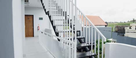 Una escalera moderna con barandillas blancas y peldaños negros, que conduce a un espacio exterior con vistas a un edificio de tejados rojos y campos verdes.