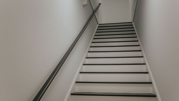 A staircase with a handrail, white walls, and a landing area.