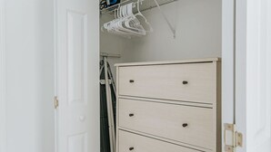 A white door with a simple handle, a white wardrobe with four drawers, and a white hanging rack with clothes.
