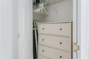 A white door with a simple handle, a white wardrobe with four drawers, and a white hanging rack with clothes.