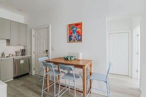 A modern kitchen with grey cabinets, a wooden dining table with four chairs, and a colorful abstract painting on the wall. - The Social Loft: Above Reunion, Walk Everywhere! (Staunton)