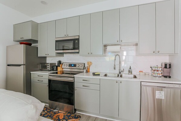 A compact kitchen with a microwave, oven, sink, and a coffee maker.