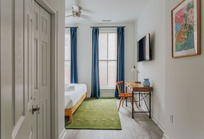 Un dormitorio con cama, escritorio, silla, televisión y ventana con cortinas.