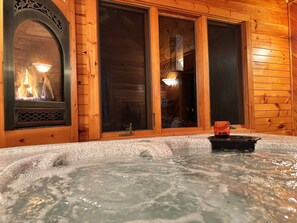 A wooden cabin interior with a hot tub, a fireplace, and large windows. - Smoky mountain views family cabin (Waynesville)
