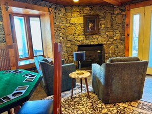 A cozy room with a stone wall, a fireplace, comfortable seating, and a green table with poker chips. - Smoky mountain views family cabin (Waynesville)