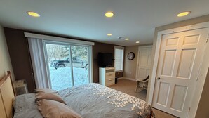 Une chambre à coucher comprenant un lit, une commode, un téléviseur et une porte donnant sur une autre pièce.