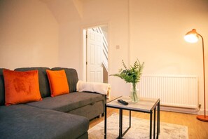 Ein Wohnzimmer mit einer Couch, einem kleinen Tisch, einer Lampe und einer Pflanze.