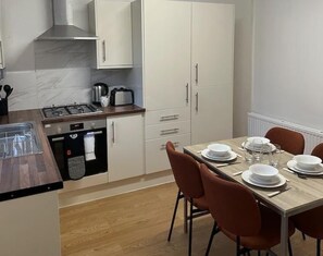 Eine moderne Küche mit weißen Schränken, einer Holz Arbeitsplatte und einem Esstisch für vier Personen.