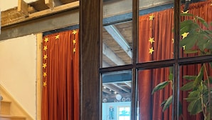 Un escalier en bois mène à une pièce dotée d’une grande fenêtre, de rideaux rouges ornés d’étoiles et d’une plante posée sur une table.