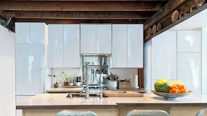 Une cuisine moderne avec des meubles blancs, un îlot central doté de tabourets, et une variété d’ustensiles et d’appareils de cuisine.