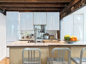 Una cocina moderna con armarios blancos, una isla central con taburetes de bar y una variedad de utensilios y electrodomésticos.