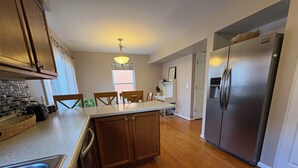 A kitchen with wooden cabinets, a stainless steel refrigerator, a dining area with chairs, and a window with blinds. - Stylish North Point Breeze Townhome, 3BR/2.5BA, Sleeps 6, Garage Parking (Pittsburgh)