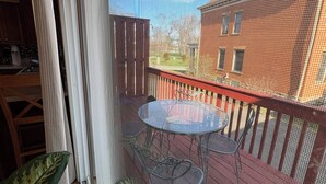 A view through a window with a metal screen, a patio with a round table and chairs, and a building in the background. - Stylish North Point Breeze Townhome, 3BR/2.5BA, Sleeps 6, Garage Parking (Pittsburgh)