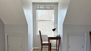 A room with a sloped ceiling, a window with blinds, a desk with a chair, and two cabinets. - Stylish North Point Breeze Townhome, 3BR/2.5BA, Sleeps 6, Garage Parking (Pittsburgh)