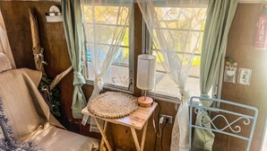 Un interior acogedor con una cama, una mesita de noche con lámpara, una ventana con cortinas y un letrero de neón arriba.