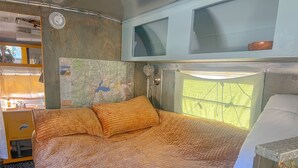 Una cama con colcha, un mapa en la pared, una ventana y un lavamanos.