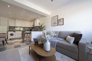 A modern living room with a sofa, coffee table, and a kitchen in the background.
