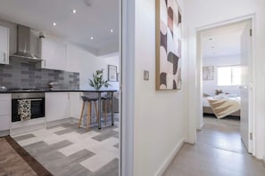 A modern kitchen with grey and white tiles, a stainless steel range hood, and a dining area with a table and chairs.