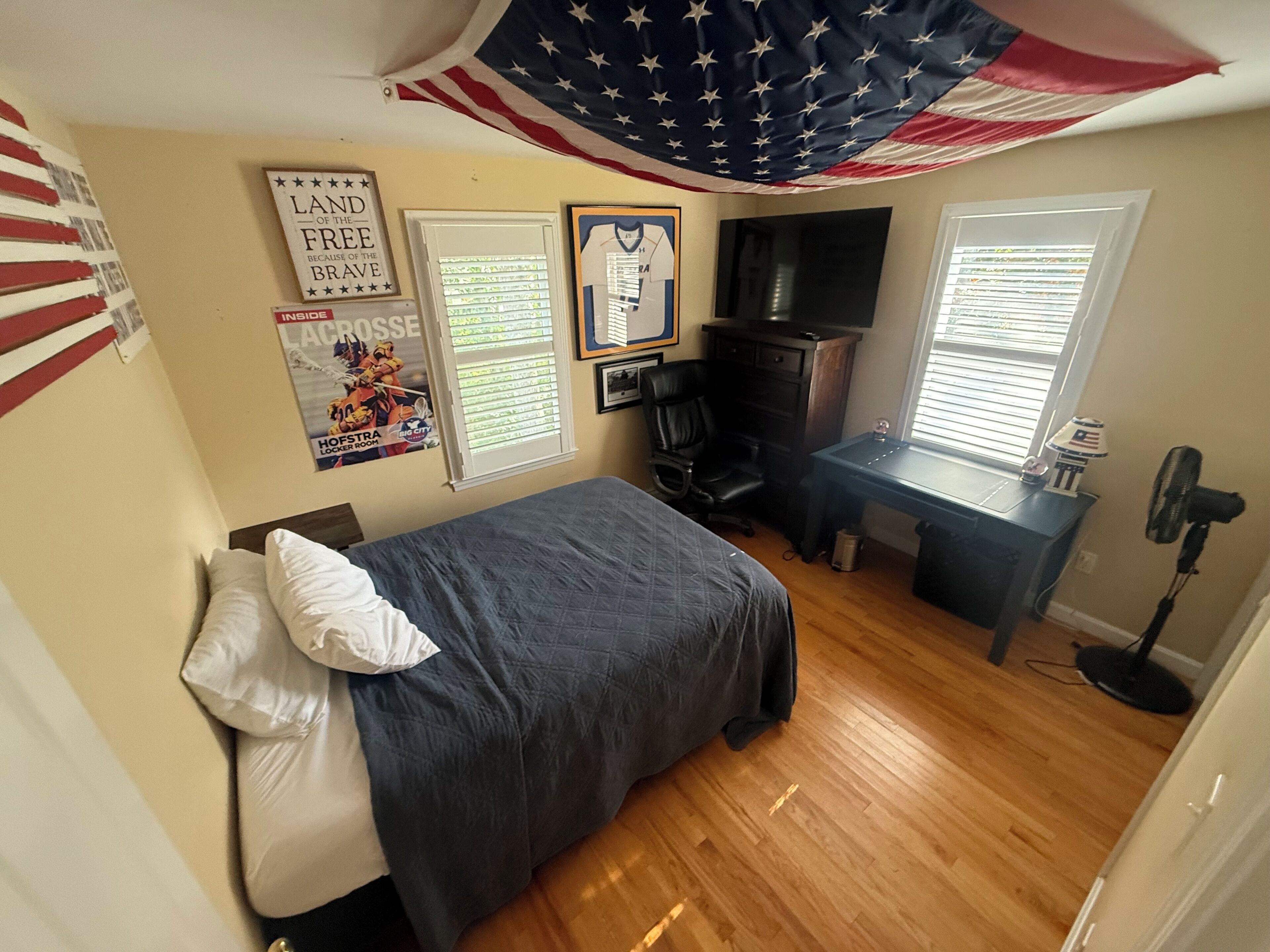 A bedroom with a bed, desk, chair, and an American flag.