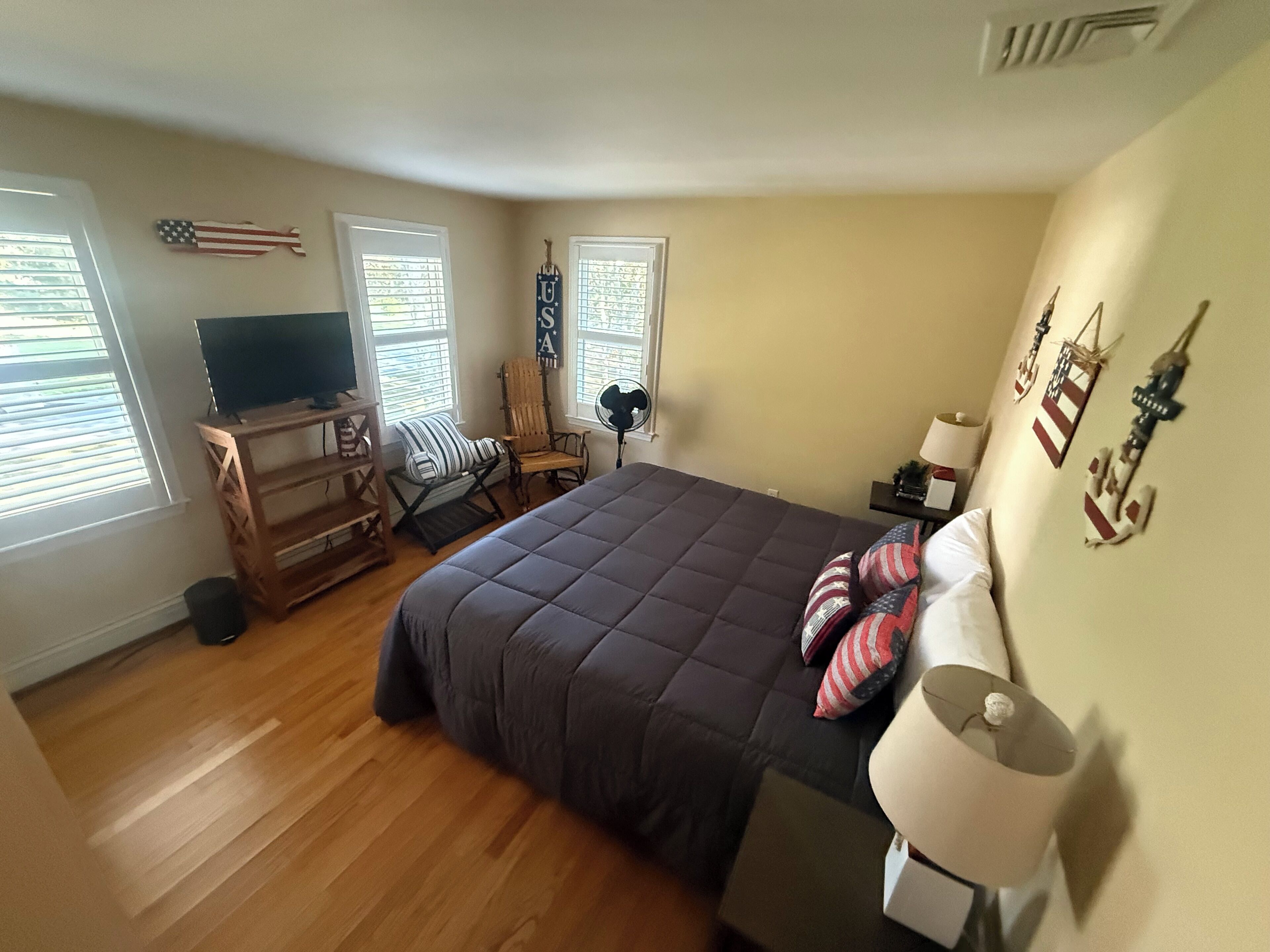 Een slaapkamer met een bed, een televisie, een stoel, een lamp en ramen met zonwering.