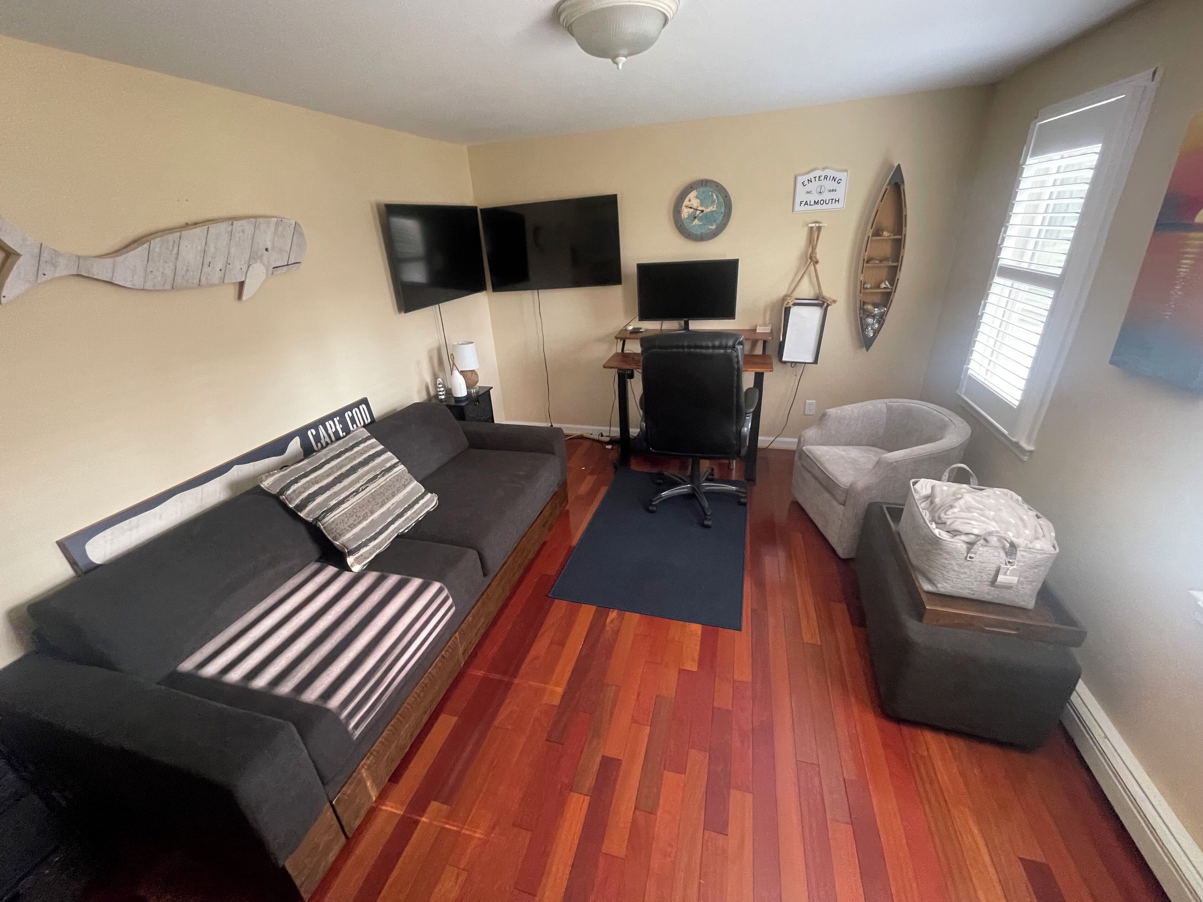 Un salon comprenant un canapé, un bureau avec un ordinateur, une chaise, une décoration murale représentant des poissons, une horloge et un panneau.