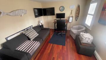 Un salon comprenant un canapé, un bureau avec un ordinateur, une chaise, une décoration murale représentant des poissons, une horloge et un panneau.