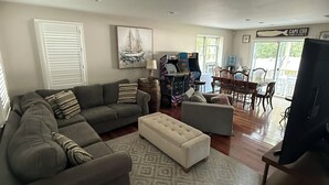 Una sala de estar con sofá, reposapiés y una mesa de centro, un comedor con sillas y una mesa, y un televisor.
