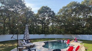 Un patio trasero con piscina, sillas de descanso y una zona de estar cubierta.