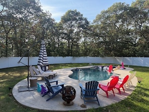 Un patio trasero con piscina, sillas de descanso y una zona de estar cubierta.