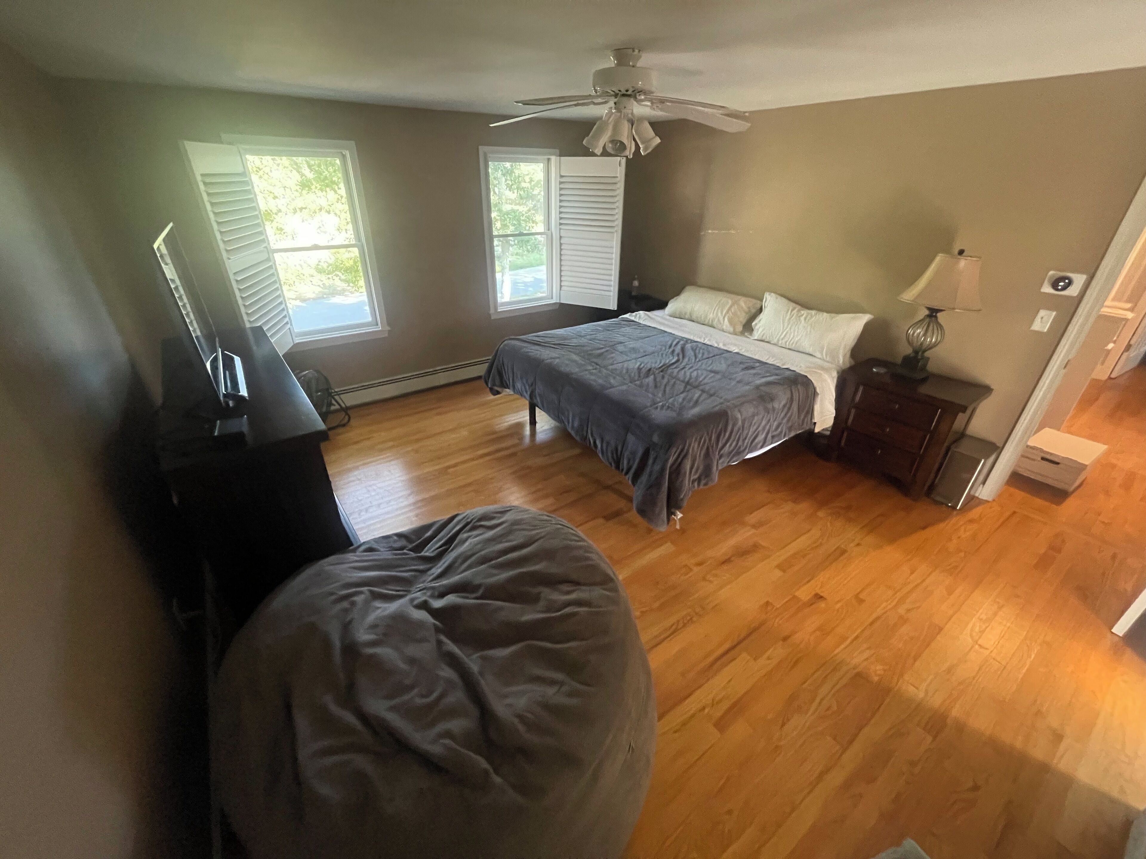 Een slaapkamer met een bed, een plafondventilator, een dressoir en een raam.