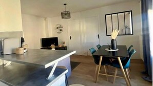 A modern kitchen with a central island, a dining area with a table and chairs, and a living area with a TV and decorative items.