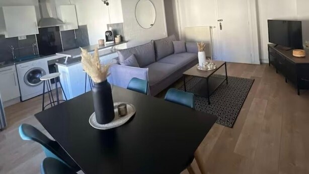 A modern living room with a sofa, dining table, and kitchen area.