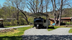 A gravel path leading to a covered RV parking area with a Minilite camper, surrounded by trees and a picnic area.