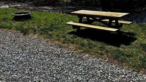 A picnic table and a fire pit in a park with trees and a river.