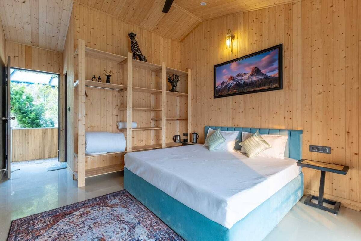 A wooden-paneled room with a bed, a shelf unit, a painting, and a view through an open door.