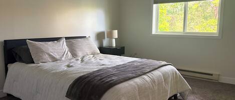A bedroom with a bed, a nightstand, a lamp, and a window with a view of trees.