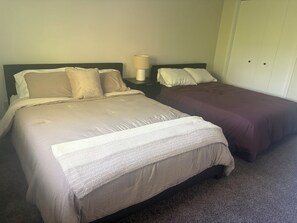 A hotel room with two beds, a nightstand with a lamp, and a wardrobe.