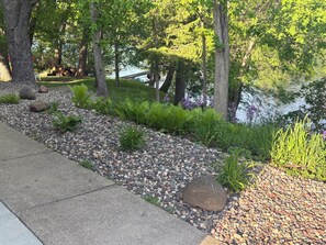 A landscaped garden with a pebble path, trees, and a water body.