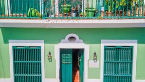Um edifício com fachada verde, duas janelas com moldura verde e uma porta com moldura verde.