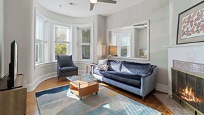 Una sala de estar con sofá, sillón, mesa de centro, chimenea y ventanas amplias.