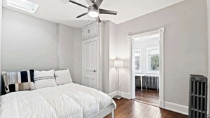 Un dormitorio con una cama, ventilador de techo, radiador y puerta que da a un balcón.