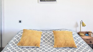 Un llit amb roba de llit estampada, dos almoines, un quadre penjat a la paret i una làmpada de nit.