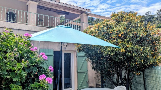 Un pati exterior amb una taula, cadires, un para-sol blau i una porta verda.
