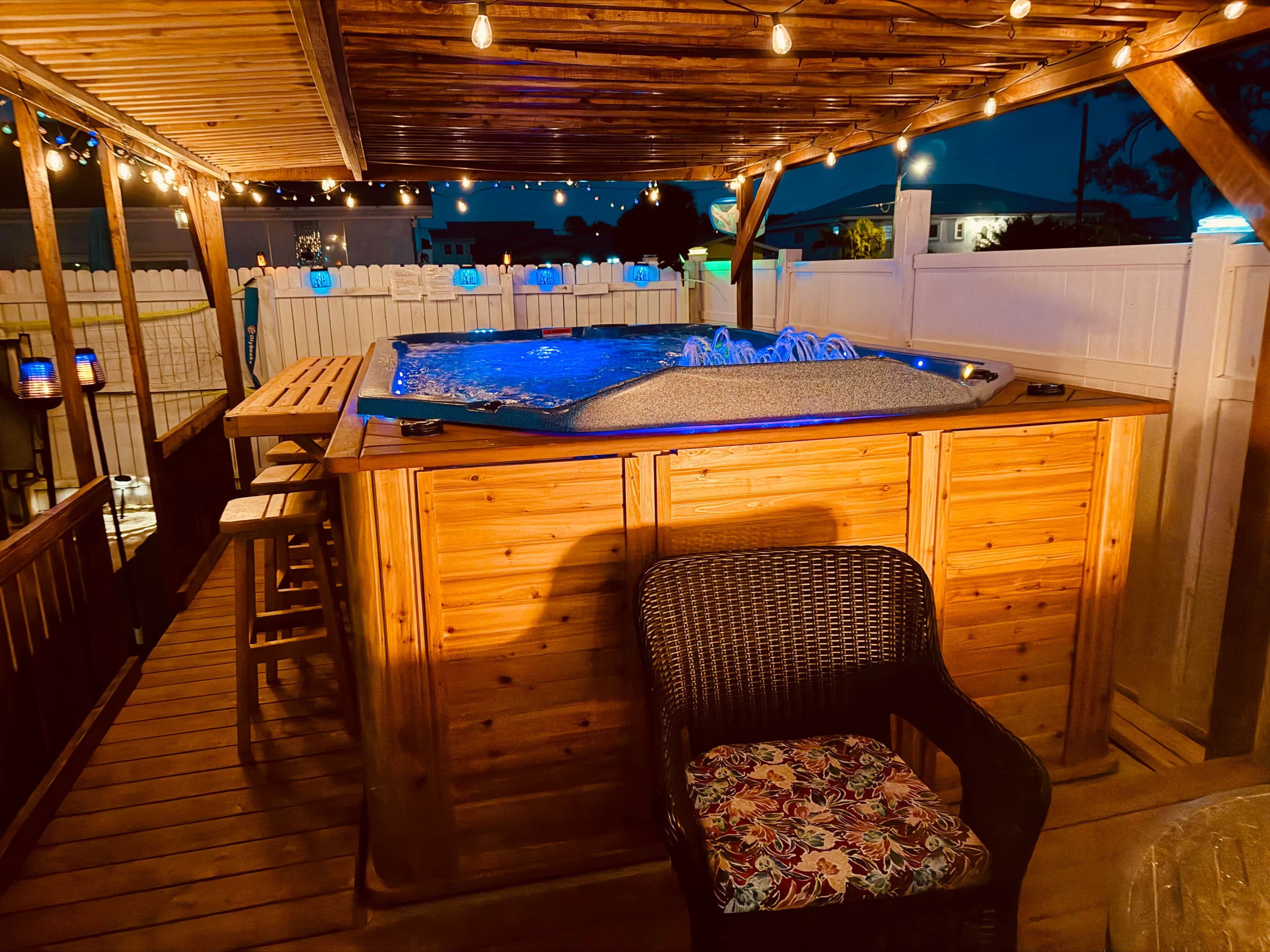 A wooden deck with a hot tub, a wicker chair, and a wooden table.