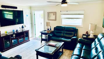 A living room with a flat-screen TV, leather sofas, a coffee table, and a ceiling fan.
