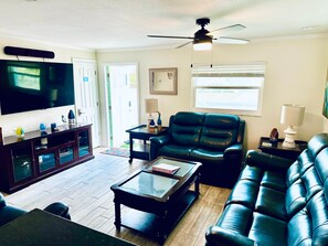 A living room with a flat-screen TV, leather sofas, a coffee table, and a ceiling fan.